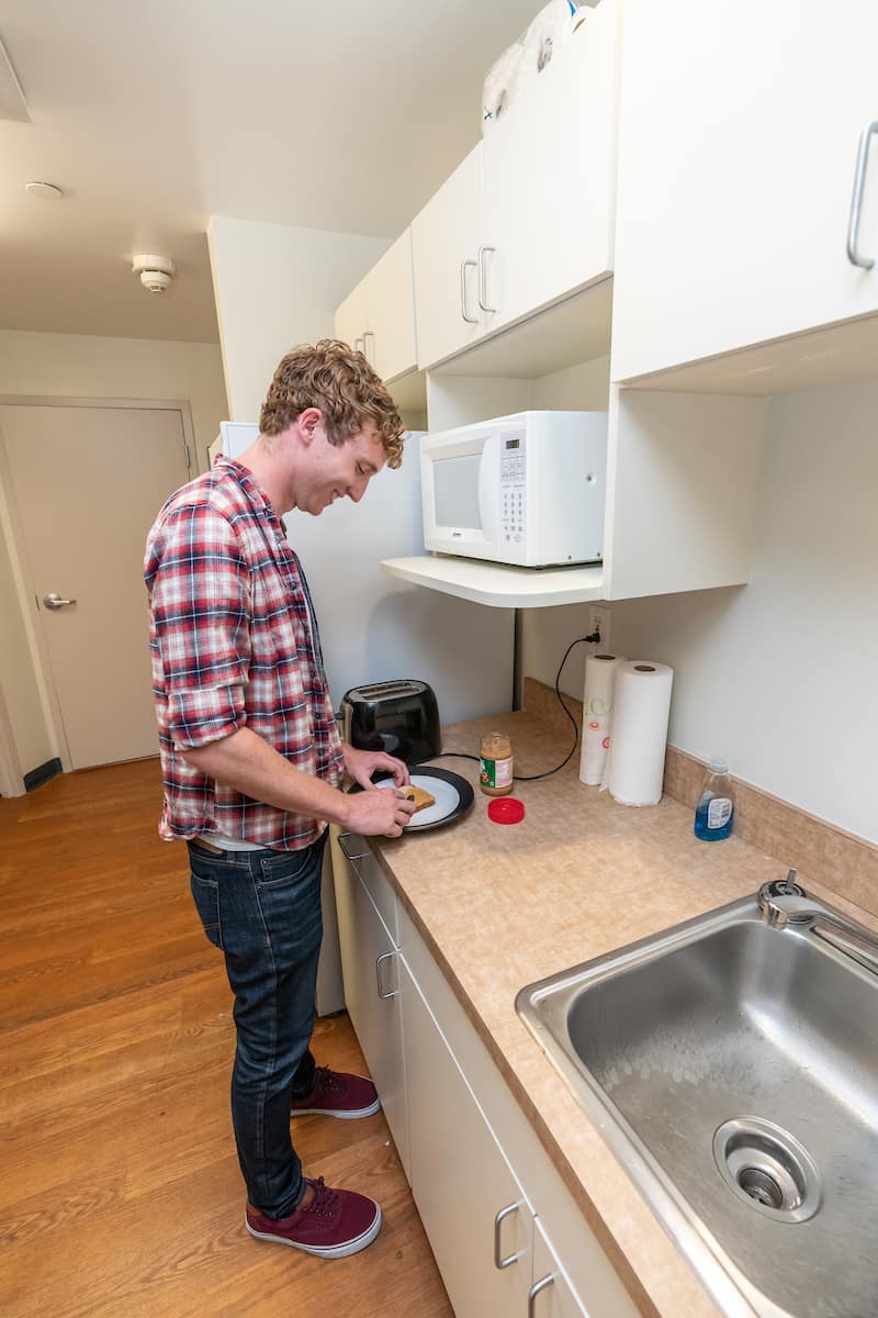 Male student prepares something in the kitchen in an Apollo Hall Room.