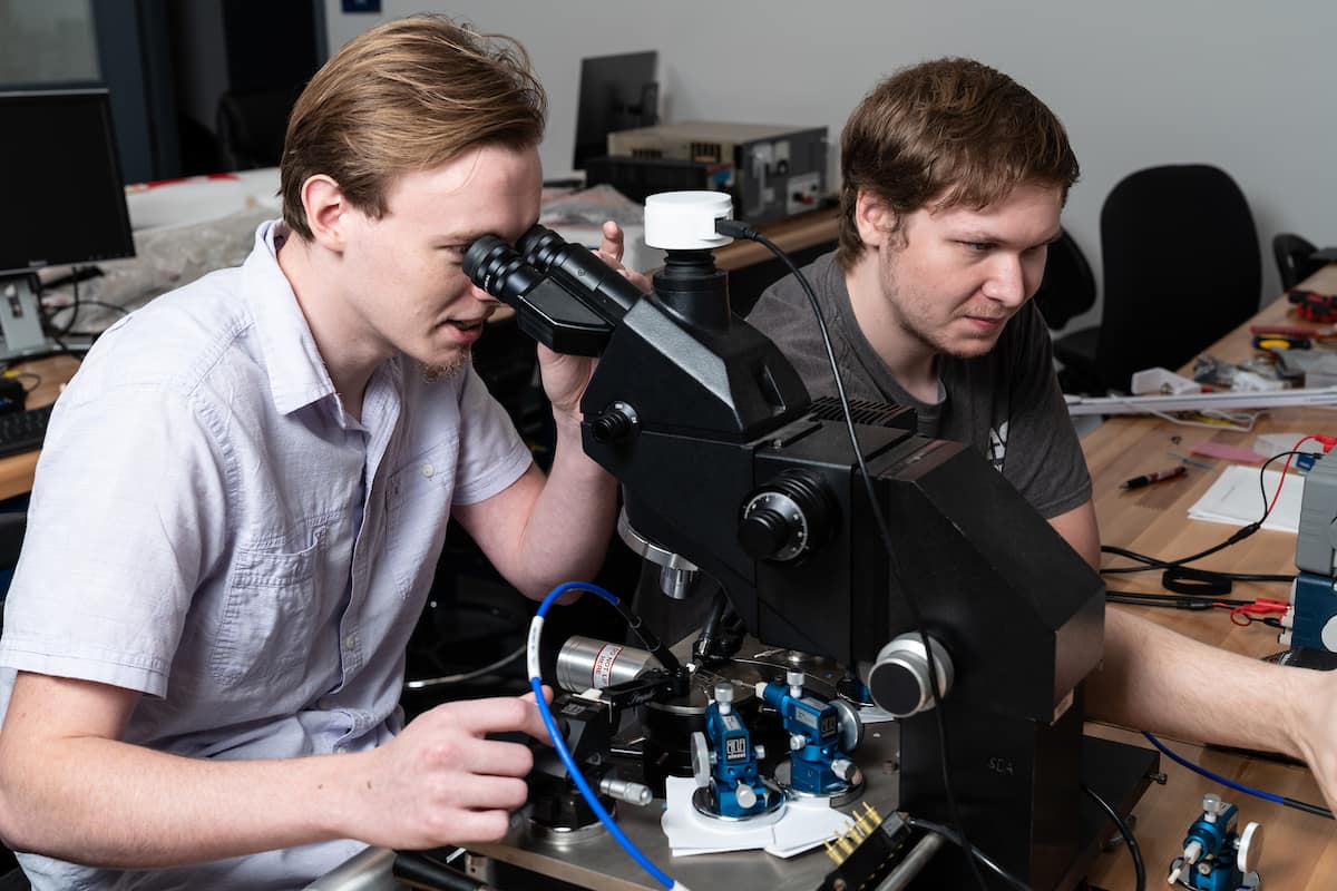 Daniel Sommer and John Sahr working with microscopes and probes to test the power properties of antenna materials.