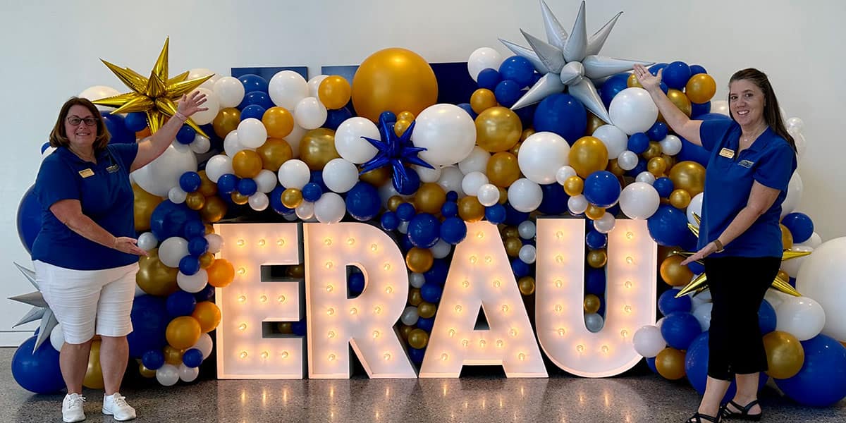 Amy Crystall poses in front of an ERAU lighted sign with fellow Advisory Council member