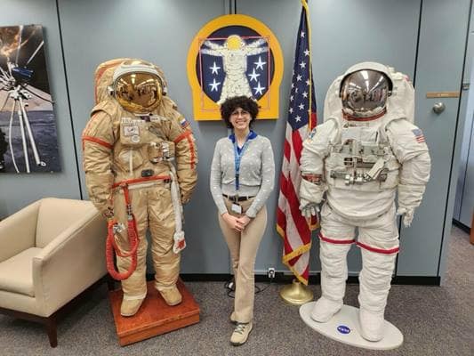 Aerospace Engineering senior Liz Bosch stands beside two spacesuits 
