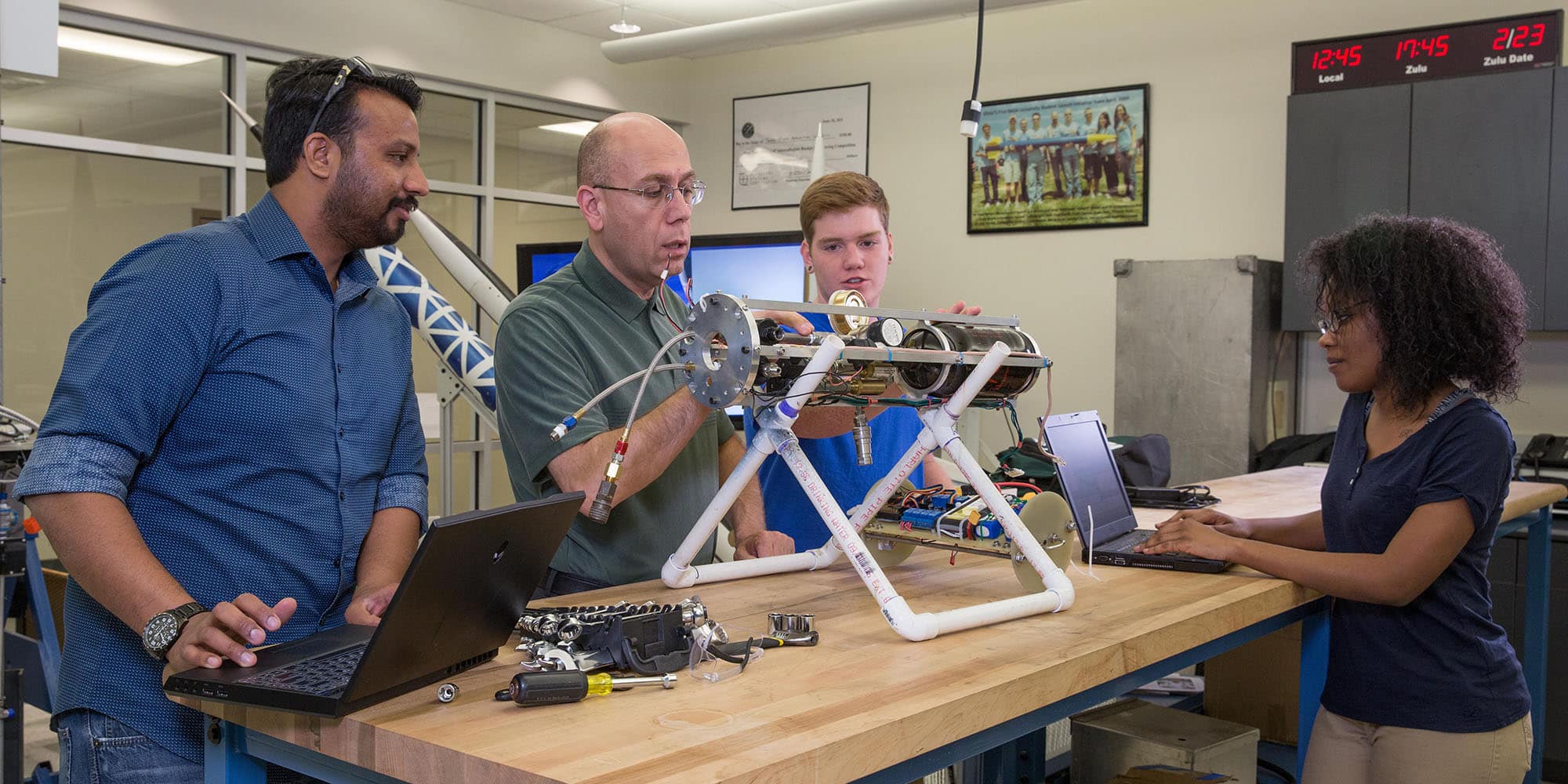 Several people stand at a table working on a piece of equipment.