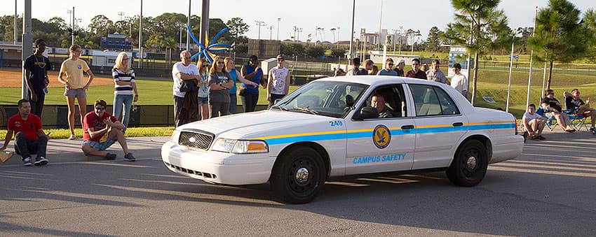 Campus safety patrol car drives down a street lined with pedestrians.