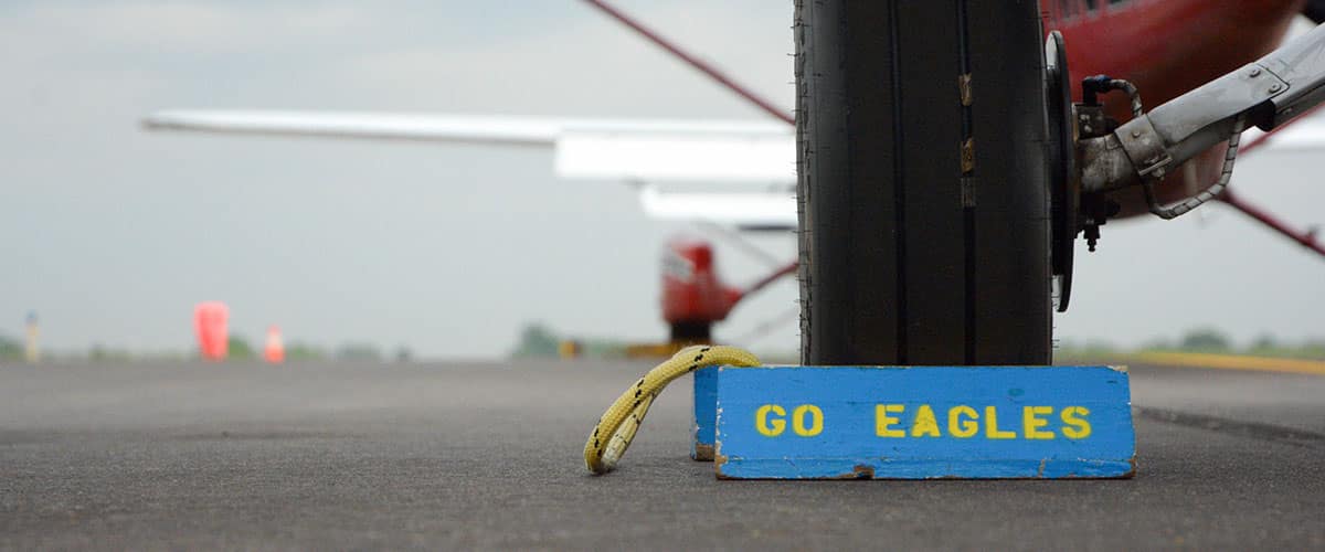 A blue and yellow chock with the words "Go Eagles" in front of an airplane tire