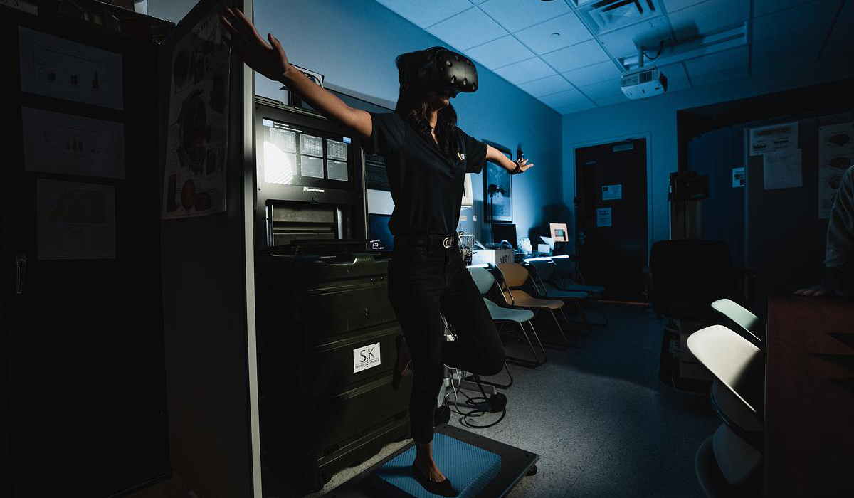 Woman balances on one foot while wearing an occulus. 