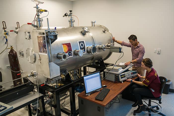 Two student researchers working with a plasma chamber