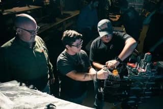 A professor and two students working on an engine.