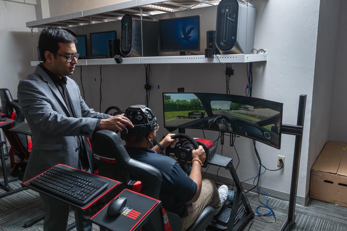 Professor and student work on a driving simulator.