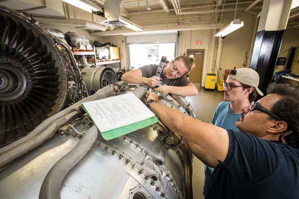 Three students working on an engine in a lab.